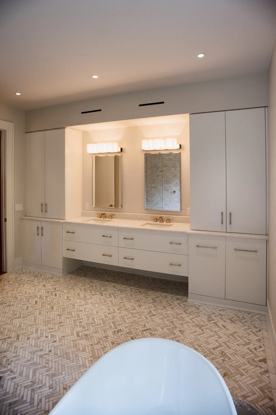 Master bath — wide view with freestanding tub, double vanity, and marble herringbone floor